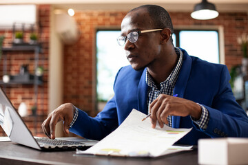 Black male entrepreneur in startup office checking business analytics on laptop. African american...