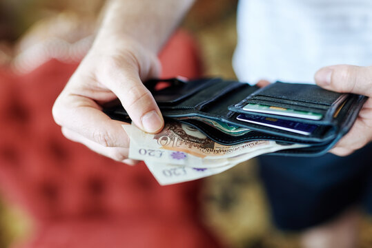 Person holding open wallet displaying british pounds and credit cards, representing concepts of personal finance, spending money, banking, and budget planning