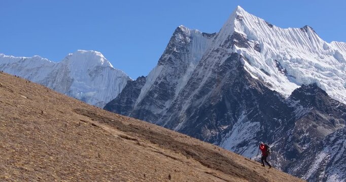 A solo traveler hikes along the Manaslu Circuit in Nepal with dramatic snow-capped Himalayan mountains rising in the background.