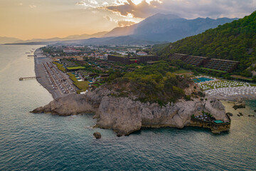 Aerial drone view of luxury beach resort on Mediterranean coastline with mountains at sunset
