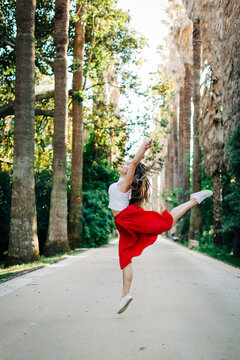Young woman jumping while dancing on road amidst trees in park