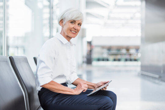 Smiling senior businesswoman sitting in waiting area using tablet