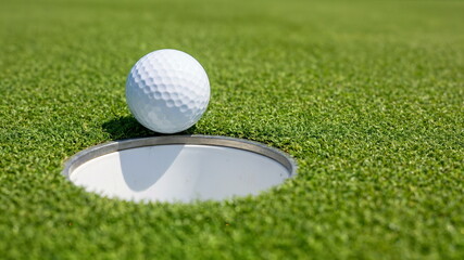 A white golf ball perfectly positioned at the edge of the hole on a vibrant green putting course, symbolizing precision and goal achievement in sports.
