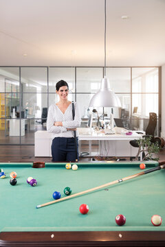 Businesswoman standing at pool table, playing billard, smiling