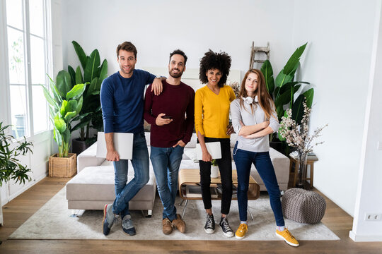 Portrait of four happy friends standing side by side in living room