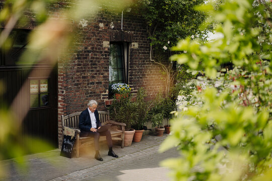 Senior businessman sitting at a farmhouse using laptop