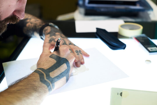 Tattoo artist designing motif on light table in studio