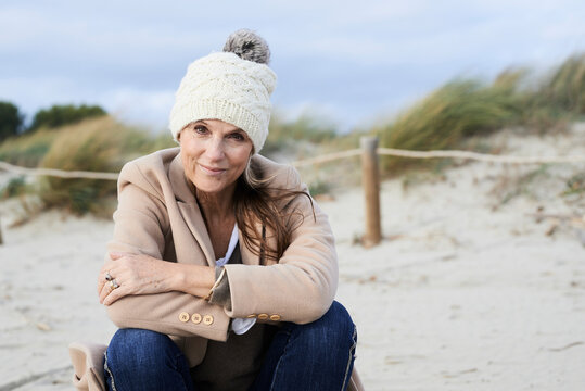 Spain, Menorca, portrait of smiling senior woman wearing bobble hat on the beach in winter