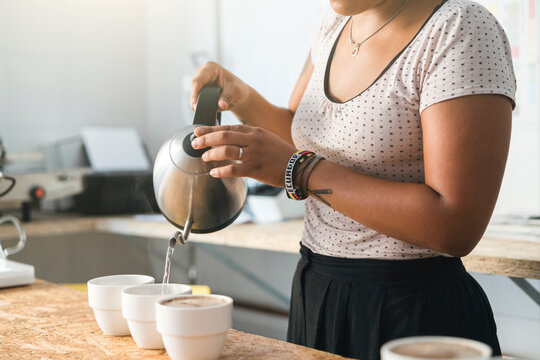 Close-up of woman working in a coffee roastery pouring hot water into coffee cups