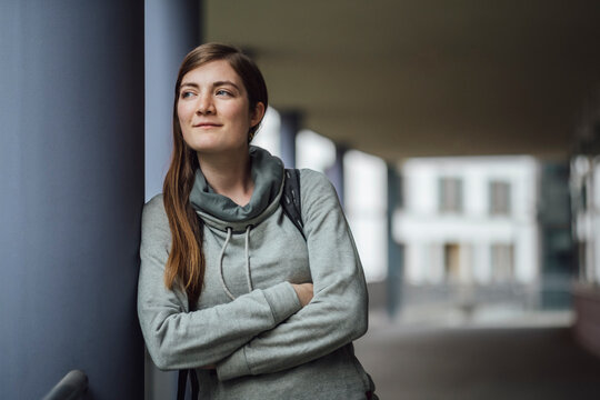 Portrait of smiling young woman leaning against column looking at distance