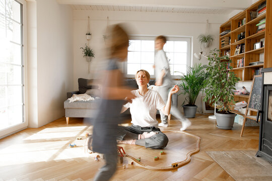 Mother meditating in the middle of toys, whilchirdren are running around her