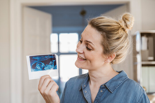 Pregnant woman holding ultrasound image at home