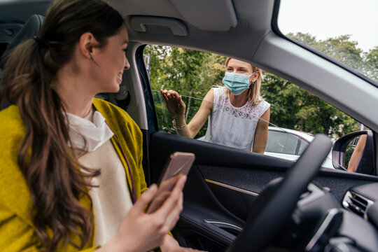 Woman wearing a protective mask talking through car window with woman without mask