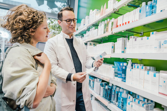 Pharmacist recommending medicine to smiling customer in chemist shop