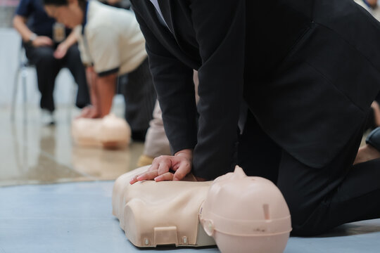 A close-up shows hands performing chest compressions on a CPR training dummy, demonstrating life-saving techniques during a first aid course.