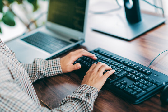 Person typing on keyboard at office desk with laptop computer, hands on keys and remote work setup for programming and productivity