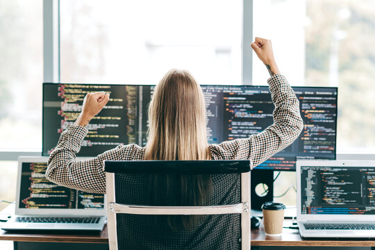 Female programmer celebrating success at a multi‑monitor coding workstation &mdash; software developer coding and debugging on laptops and screens with coffee cup