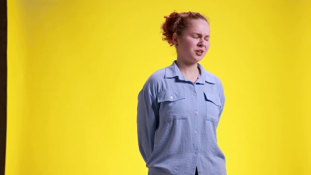 Young woman showing disgusted facial reaction while standing on yellow studio background. Concept of product rejection, negative review, customer dissatisfaction and unpleasant experience.