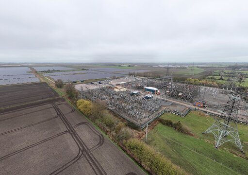 Aerial view of a substation with battery energy storage systems and solar farm, contrasting urban infrastructure with the surrounding rural landscape, Burwell, United Kingdom.