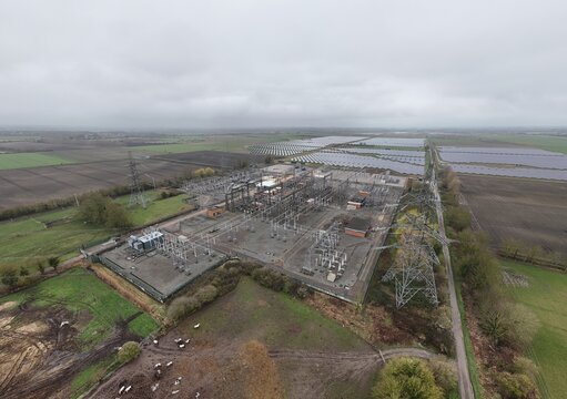 Aerial view of electrical substation contrasting with the adjacent solar farm under a cloudy sky, Burwell, United Kingdom.