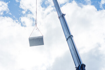 Obraz premium Heavy metal slab suspended from a crane against a cloudy sky at a construction site, showcasing the precision and effort in urban development and engineering challenges