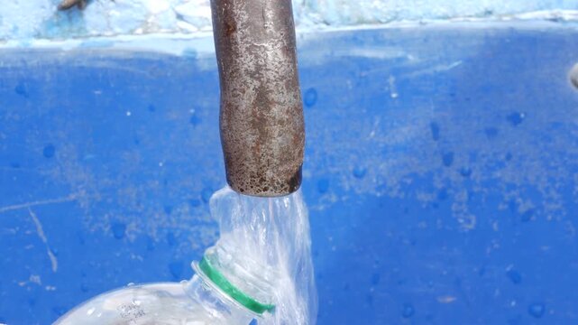 Person filling a plastic bottle with water from a metal pipe