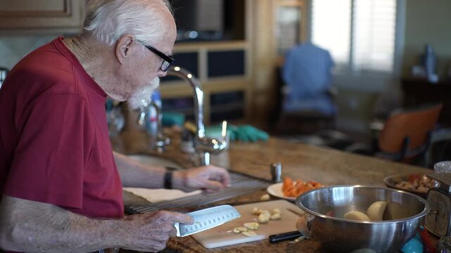 Senior man mashes and minces garlic in his kitchen while preparing his meal and enjoying the cooking process.
