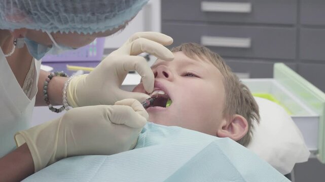 Dentist treats a boy with a chipped tooth. The dentist carefully applies a special glue to the chipped area to attach a broken tooth fragment