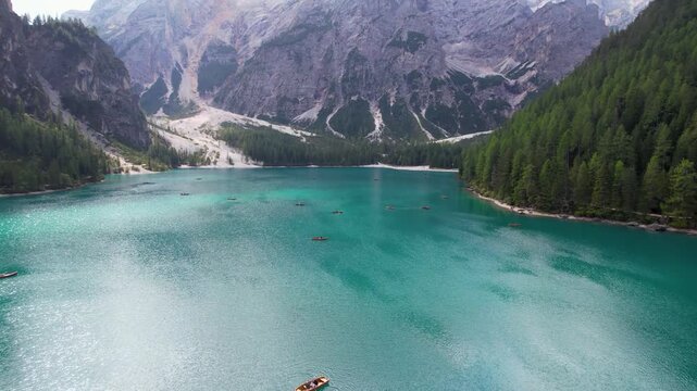 Aerial view of boats scattered across the turquoise waters of Lago di Braies, surrounded by towering mountains and lush forests, Dobbiaco, Trentino-South Tyrol, Italy.