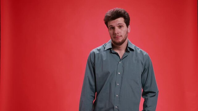 Young man nodding with indifferent expression on red studio background. Concept of passive agreement, lack of interest, bored reaction, polite acknowledgment and minimal engagement in conversation.
