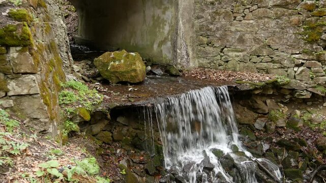 Small waterfall flowing from stone viaduct culvert