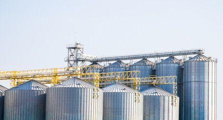 Steel grain storage silos with a conical bottom can be used for various purposes. Industrial facilities of feed and flour mills. Against the backdrop of a beautiful sky with clouds. © Rangsarit