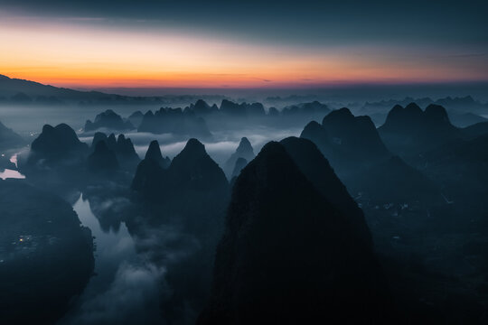 Aerial view of dramatic karst mountains piercing through the misty veils under the warm glow of the setting sun, Guilin, China.