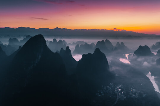 Aerial view of jagged karsts pierce through the ethereal mist-shrouded landscape, bathed in the warm glow of the rising sun, Guilin, China.
