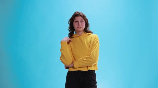 Young woman slowly nodding with bored indifferent expression on blue studio background. Concept of passive agreement, lack of interest, tired reaction, polite listening and emotional disengagement.