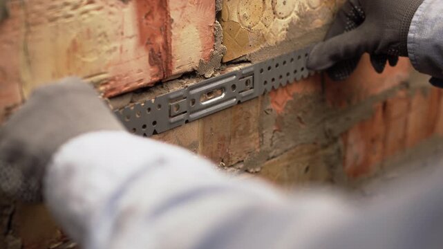 Female construction worker fixing galvanized steel drywall hangers for metal profiles on brick wall.