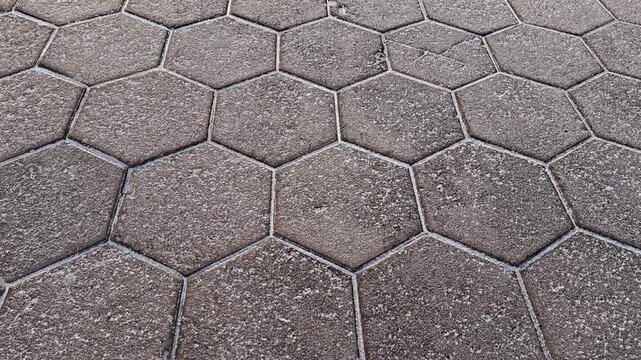 The sidewalk is paved with gray, hexagonal concrete slabs. The slabs are covered with snow. The sidewalk serves as texture