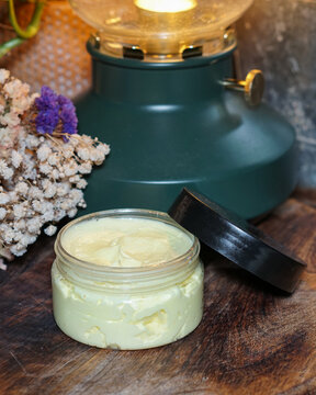 Vertical image of homemade face or body cream with turmeric in transparent jar on dark wooden background with dry flowers. Natural skincare and clean beauty concept.