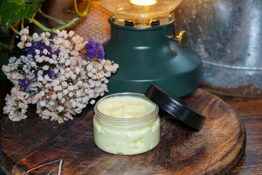 Homemade face or body cream with turmeric in transparent container on dark wooden background with dry flowers and soft light. Natural skincare and herbal cosmetic concept.