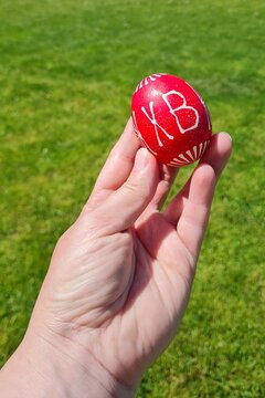 Red egg with white design held in hand on green grass during sunny day