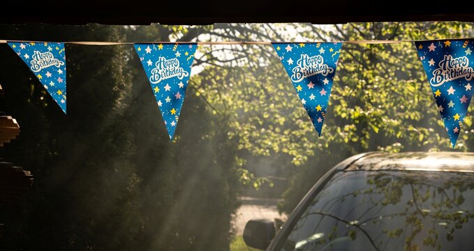 Colorful birthday decorations hang in the sunlight outside a home during a celebration