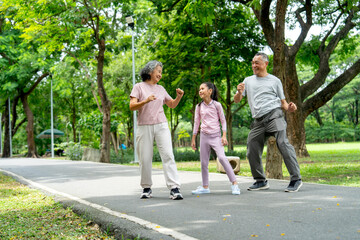 Fototapeta premium Asian senior man and woman also the girl action of stretching the legs and they look happy in public park together.