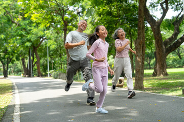 Fototapeta premium Front view of Asian girl run ahead senior man and woman in the competition between them in public park and they look happiness that have good time together.