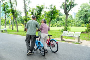 Obraz premium Back of Asian senior woman and man leading the bicycles on the road together in the public park with day light and they look happiness.