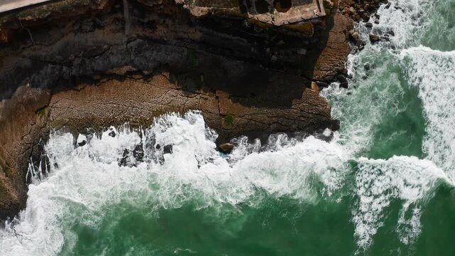 Aerial view of the beautiful ocean rocky shore with rolling waves.  Drone hovers over surface of the water along the rocky shore. Drone is hovering over rolling ocean waves to the rocky shore.
