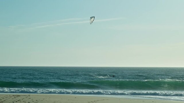 Sportsman go kitesurfing in Atlantic Ocean, slow motion. Extreme sports, skateboarding on vacation on sandy beach in windy weather. Extreme Kitesurfing. Man Kite Surfing Against blue Sky.