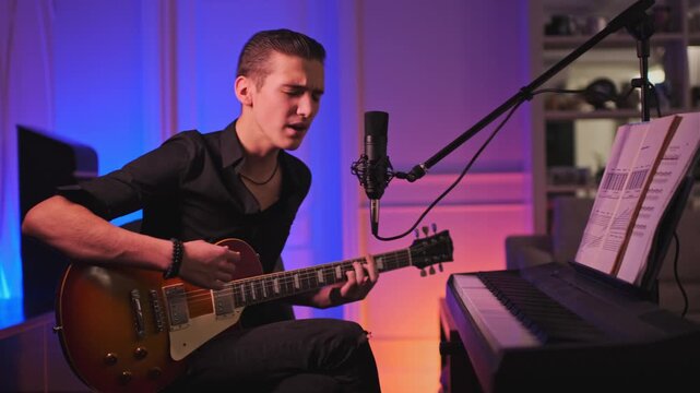 Cinematic footage of teenager plays rock on a guitar. Teen boy plays a musical instrument.  Young man sings and plays the electric guitar at home. Musician records his composition in a music studio.