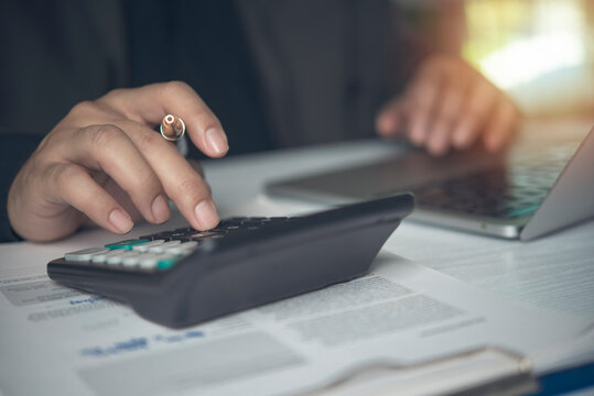 Accountant hands using calculator holding pen computing financial data clipboard paperwork laptop desk. Business finance tax auditing accounting economy investment planning budget.