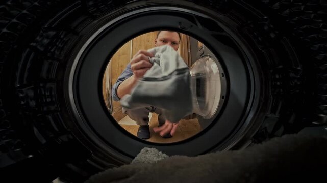 A man engages in household chores, removing freshly washed clothes from the washing machine drum in the bathroom, completing a crucial step in the laundry cleaning process