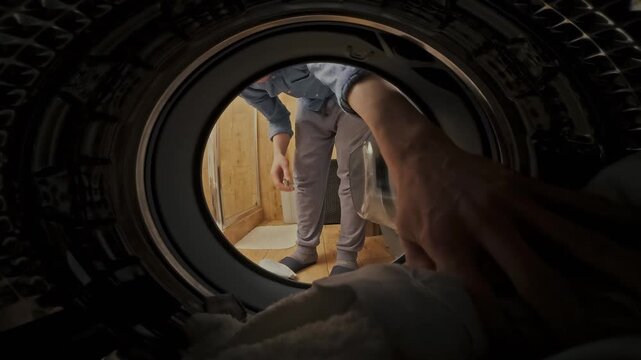 A man loads soiled garments into a laundry machine at a public laundromat, initiating the wash cycle as part of routine domestic duties, fulfilling household cleaning needs